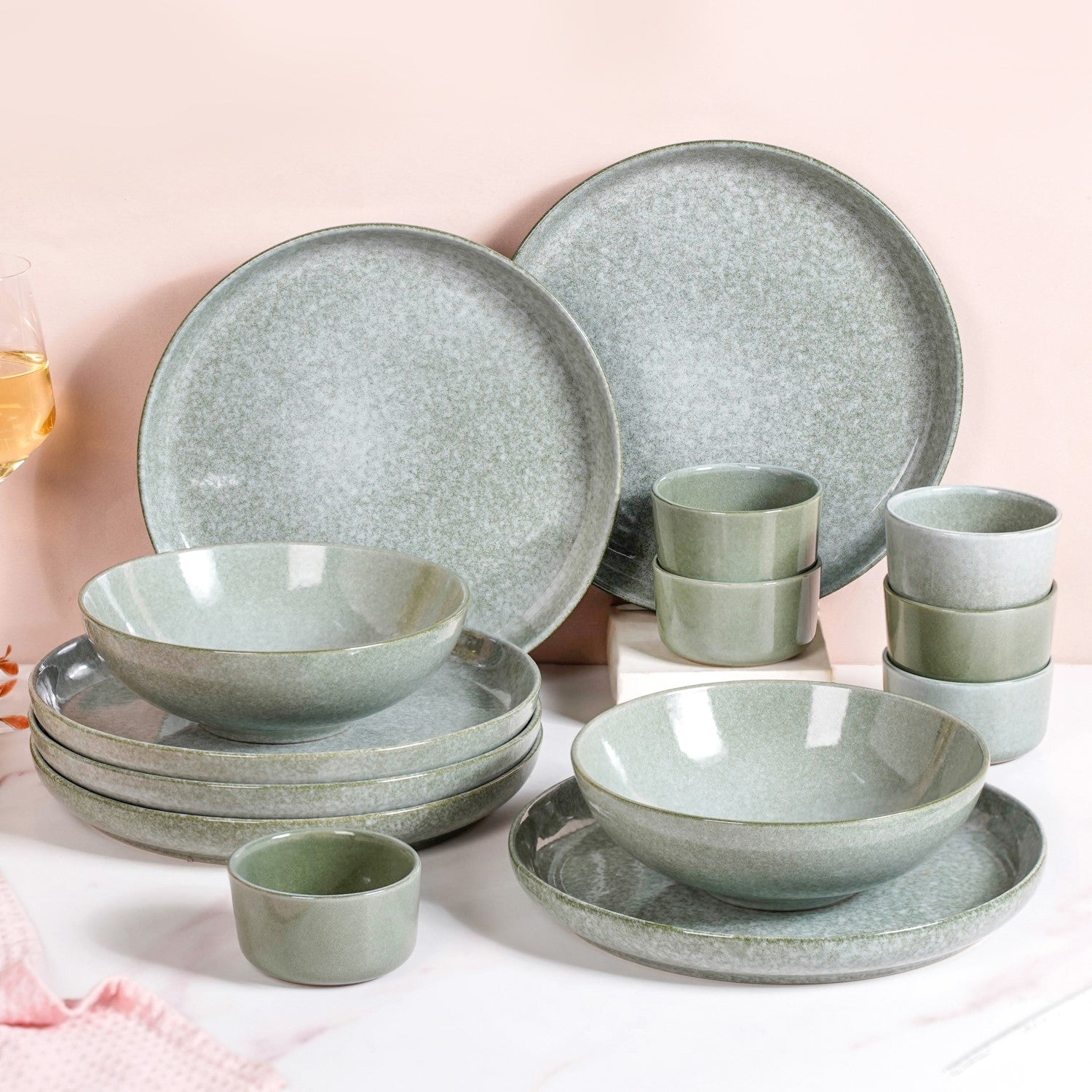 Set of green ceramic dinnerware on a light pink background