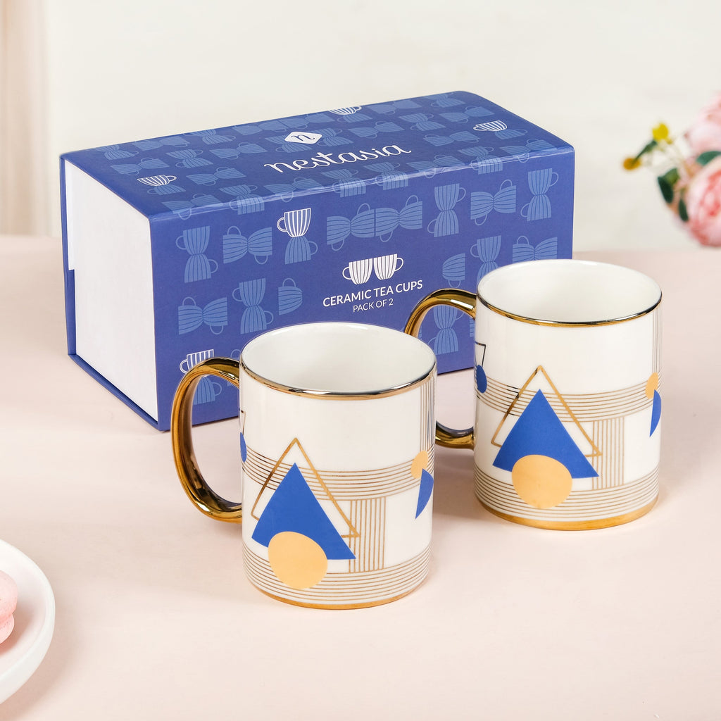 Two ceramic tea cups with geometric designs on a white surface, next to a branded box.